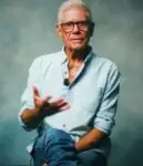 ron piana being interviewed on white underbelly youtube sat in navy jeans and a sky blue shirt with black rimmed glasses